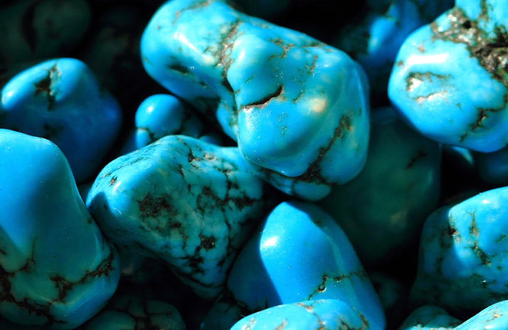 Vibrant blue, polished turquoise stones with dark vein patterns clustered together in a close-up arrangement.