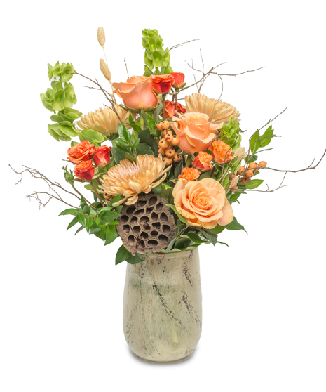 Vase arrangement with peach and orange flowers, accented with woodland branches, berries, and lotus pods, capturing the warm, amber tones of autumn.