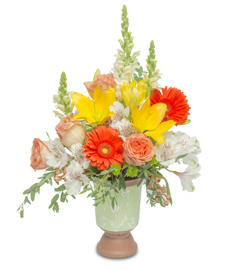 Terracotta pedestal with snapdragons, gerbera daisies, lilies, and roses, accented with apricot berries and green button mums, evoking the warm hues of a sunset.