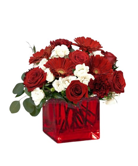 A romantic floral centerpiece featuring red roses, burgundy carnations, red gerbera daisies, ivory spray roses, and flowing greenery like eucalyptus and ruscus.