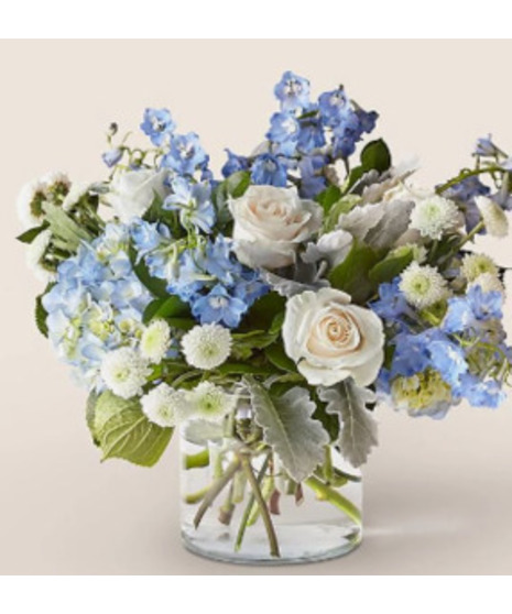 Elegant floral arrangement with blue hydrangea, white roses, delphinium, and button poms in a clear glass vase, designed by Walter Knoll Florist