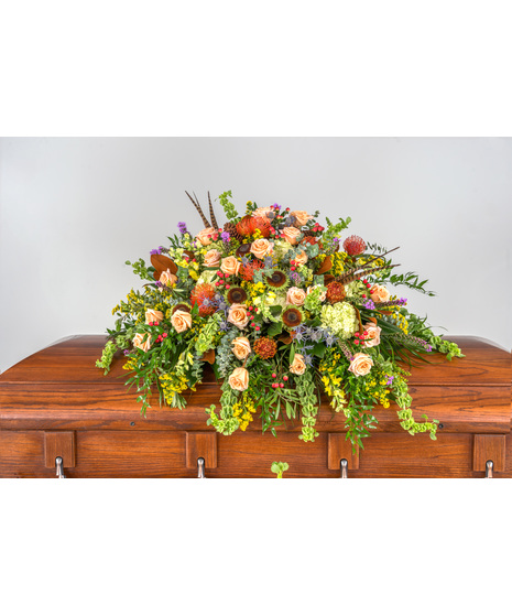 Rustic Remembrance Casket Piece, bold sunflower centers, peach roses, liatris, goldenrod, magnolia leaves, proteas, thistle, and red berries