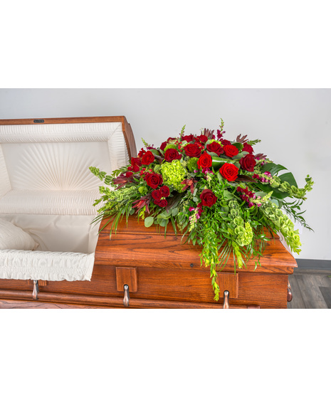 Elegant Ruby Wishes Tribute Casket Spray, featuring red roses, hydrangeas, berries, and tropical foliage—a heartfelt farewell.