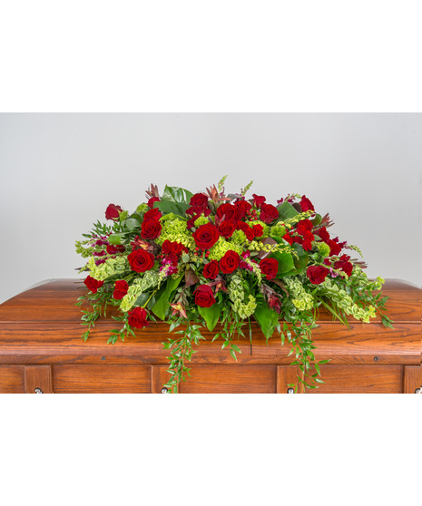 Elegant Ruby Wishes Tribute Casket Spray, featuring red roses, hydrangeas, berries, and tropical foliage—a heartfelt farewell.