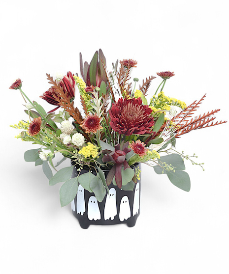 Ghostly Blooms bouquet with Rust mums, yellow goldenrod, red leucadendrom, eucalyptus, and tinted gravellia in a black pot