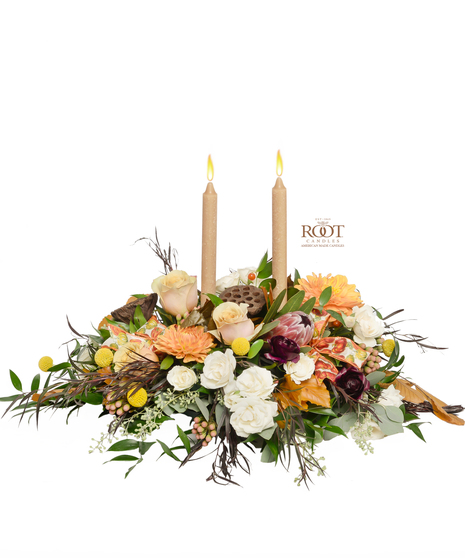  centerpiece with ivory roses, burgundy ranunculus, Mink Protea, orange dahlias, dried accents, and Root candles in a luxurious fall arrangement