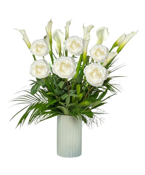 A tall white vase holds ten elegant white calla lilies with lush tropical foliage, accented with white roses in deluxe and premium styles.