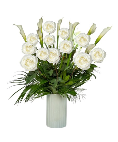 A tall white vase holds ten elegant white calla lilies with lush tropical foliage, accented with white roses in deluxe and premium styles.