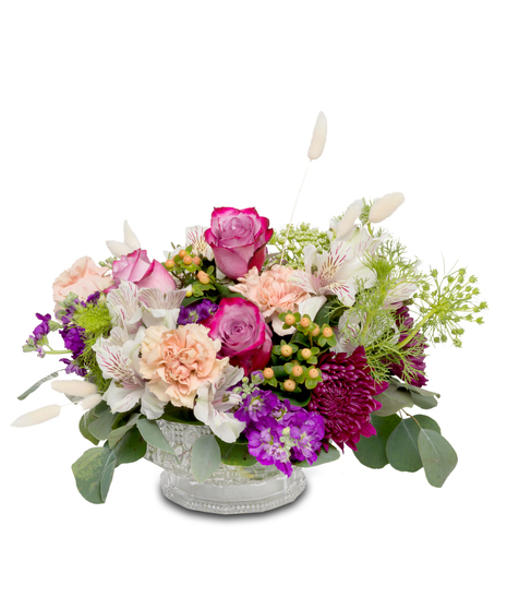 A clear dish filled with vibrant alstromerian lilies, lavender roses, purple stock, berries, and 