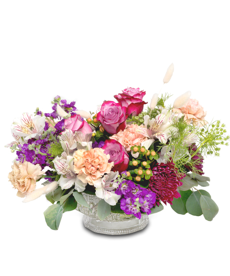 A clear dish filled with vibrant alstromerian lilies, lavender roses, purple stock, berries, and 