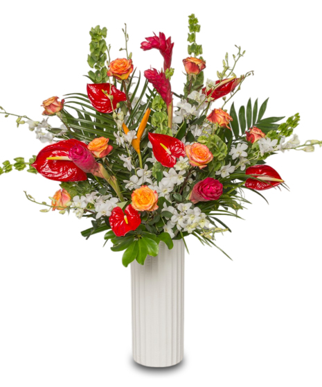 A large tropical floral arrangement in a tall white ceramic vase featuring vibrant red anthuriums, white orchids, gingers, orange roses, and lush greenery.