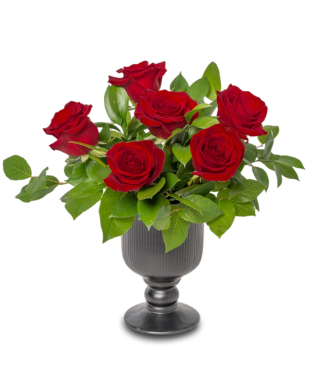 Gatsby Roses arrangement with red roses, lush ruscus and lemon leaf greenery, baby’s breath, in a black pedestal ceramic vase. Elegant Gatsby-inspired centerpiece.