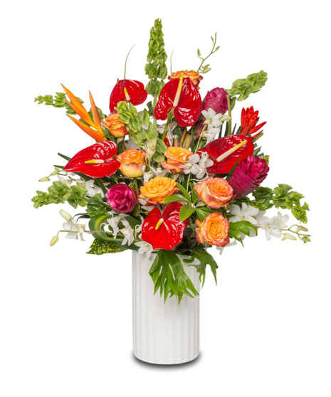 A vibrant tropical floral arrangement in a sleek white ceramic vase featuring red anthuriums, white orchids, gingers, and lush greenery.